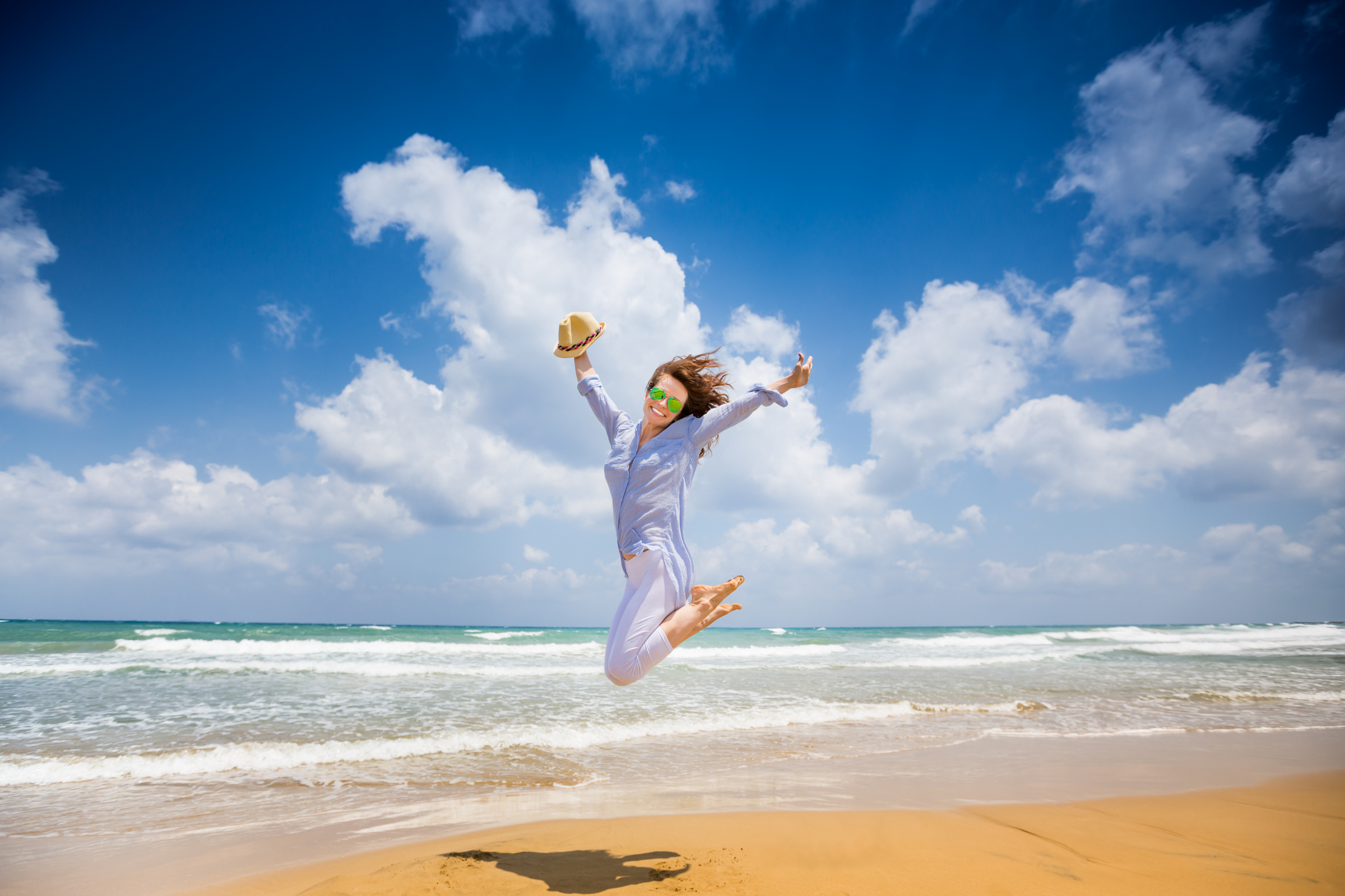 smiling woman jumping in the air on a beach.